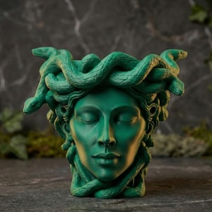K&ouml;nnte beinhalten: Ein gr&uuml;ner Medusa-Kopf-Pflanztopf mit geschlossenen Augen und einem ruhigen Ausdruck. Der Pflanztopf weist aufwendig geformte Schlangen anstelle von Haaren auf. Die Skulptur ist ein dekorativer Artikel.