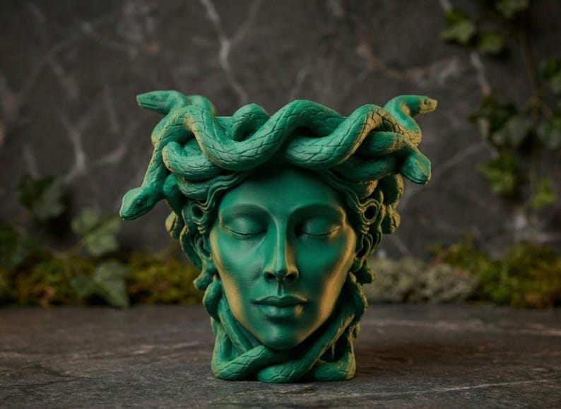 K&ouml;nnte beinhalten: Ein gr&uuml;ner Medusa-Kopf-Pflanztopf mit geschlossenen Augen und einem ruhigen Ausdruck. Der Pflanztopf weist aufwendig geformte Schlangen anstelle von Haaren auf. Die Skulptur ist ein dekorativer Artikel.