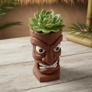 May include: A brown tiki-style planter with a green succulent plant. The planter has a carved face with white eyes and a wide grin. The planter is on a wooden surface.