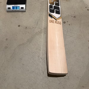 May include: A wooden cricket bat with a yellow handle and a black and gold design. The bat has the text "SS" and "DRE RUSS" printed on it.