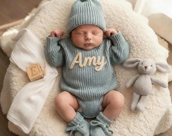 Może przedstawiać: Noworodek w jasnoniebieskim dzianinowym stroju, w tym czapka z pomponem, śpioch z imieniem "Amy" w kremowych literach i pasujące buciki. Szara pluszowa króliczka i drewniany klocek są w pobliżu.