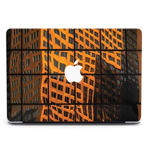 Puede incluir: Funda para portátil con un diseño abstracto del reflejo de un edificio. La imagen está dividida en secciones rectangulares, con tonos cálidos de naranja y marrón. Un logotipo blanco de Apple está centrado en la parte superior del portátil.
