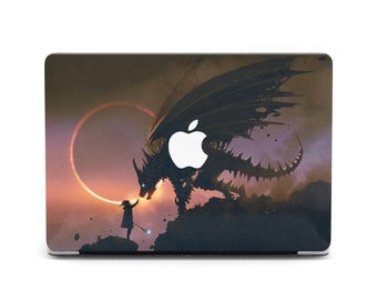 May include: A laptop skin with a dark fantasy design featuring a silhouette of a dragon with a glowing red eye, a small human figure, and a crescent moon in a dark sky.
