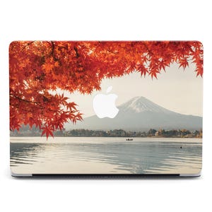 Puede incluir: Funda para portátil con una vista panorámica de un lago y una montaña nevada bajo un cielo despejado. El diseño incluye vibrantes hojas de arce rojas, con el logotipo de Apple visible.