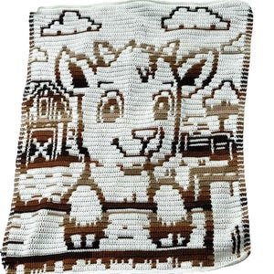 May include: A handmade crochet blanket featuring a cartoon cow design in shades of brown and white. The blanket depicts a cow, a barn, and clouds. The blanket is made of soft yarn and is perfect for a baby or child.