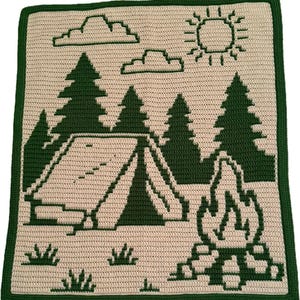 May include: A crocheted blanket featuring a camping scene. The design includes a tent, trees, a campfire, clouds, and a sun, all in dark green against a beige background. The blanket has a dark green border.