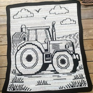 May include: A crocheted blanket featuring a black and white tractor design. The blanket has a black border and depicts a tractor with clouds and birds in the sky. The design is detailed and suitable for a nursery or as a decorative piece.