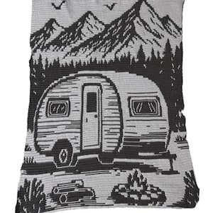 May include: A rectangular crochet blanket featuring a two-tone gray and black design. The pattern depicts a vintage camper trailer parked in front of a forest and mountain range, with two birds flying above and a campfire in the foreground.
