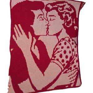 May include: A rectangular crochet throw blanket featuring a two-tone design in deep red and light pink. The pattern depicts two figures in profile facing each other in a close embrace, with one figure wearing a garment featuring a polka dot pattern.