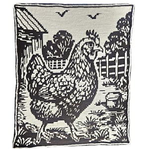 Puede incluir: Una manta de ganchillo en blanco y negro con una gallina en una escena de granja. La manta representa una gallina, un granero, una valla y árboles. La combinación de colores es un fuerte contraste de blanco y negro.