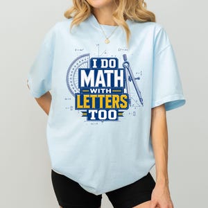Könnte beinhalten: Ein hellblaues Kurzarm-T-Shirt mit einem Grafikdruck, der den Text I DO MATH WITH LETTERS TOO in Weiß und Gelb zeigt. Das Design enthält einen blauen Winkelmesser und einen Zirkel, umgeben von verschiedenen mathematischen Formeln in feinen Linien.