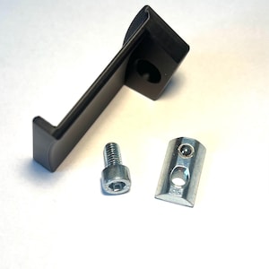 Op de afbeelding: Een zwarte metalen beugel met een gat in het midden, een zilveren T-moer en een zilveren schroef met een vierkante kop.