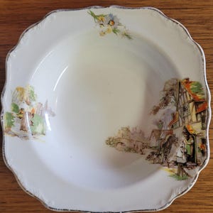 May include: A white ceramic bowl with a scalloped rim and a floral design. The bowl features a cottage scene with a house, trees, and a bridge. The bowl is decorated with gold trim.
