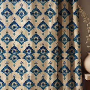 Op de afbeelding: Gordijnpaneel met een herhalend patroon van blauwe oogvormige ontwerpen op een crèmekleurige achtergrond. De oogmotieven bevinden zich in ruitvormen, waardoor een geometrisch en artistiek textiel ontstaat.