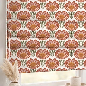 Può includere: Una tenda a rullo a motivi floreali con un motivo ripetuto di fiori arancioni e pesca stilizzati con foglie verdi su sfondo bianco. La tenda è parzialmente abbassata, rivelando una finestra e un interno decorativo.