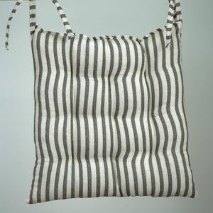 May include: A white and black striped cushion with a tie closure. The cushion is made of a soft, woven fabric and has a quilted design.