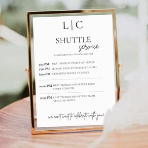 May include: A white sign with black text in a gold frame, announcing a shuttle service for a wedding. The sign lists the times for the first and second trolley pickup at the hotel, the ceremony start time, and the departure times from the venue to the hotel. The sign also includes the text "we can't wait to celebrate with you!"