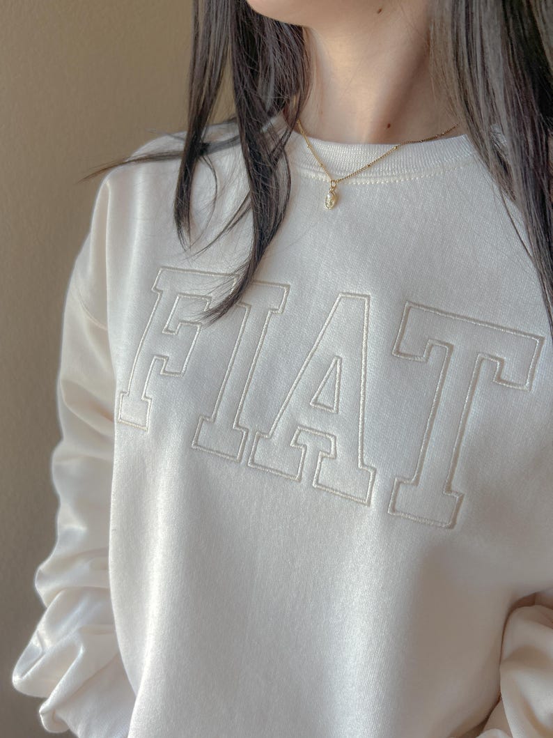 Pu&ograve; includere: Una felpa bianca con la parola "FIAT" ricamata in un grande e audace font. La felpa ha una vestibilit&agrave; rilassata e un collo rotondo.