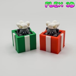 May include: Two 3D-printed cat figurines in gift boxes. One box is green with white stripes, the other is red with white stripes. Each cat is gray with a white flower on its head. The text "FLEX 3D" is at the top.