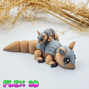Puede incluir: Un juguete de armadillo articulado impreso en 3D en color beige y gris. El juguete tiene un cuerpo segmentado, un pequeño armadillo montado en su espalda y el texto "FLEX 3D" en un degradado verde y rosa.