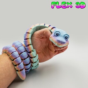 May include: A 3D-printed articulated snake toy in pastel shades, wrapped around a wrist and hand. The snake's body is a gradient of blue, purple, and orange, with a light blue head. The text "FLEX 3D" is in the upper right corner.