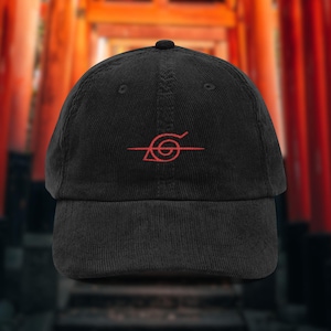 May include: Black corduroy baseball cap featuring a red embroidered symbol. The cap has a curved peak and a button on top. The design is a stylized eye with a horizontal line.