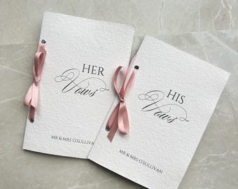 May include: Two white paper booklets with pink ribbon ties. The top booklet says "HER Vows" and the bottom booklet says "HIS Vows". Both booklets have the text "MR & MRS O'SULLIVAN" printed on the bottom.