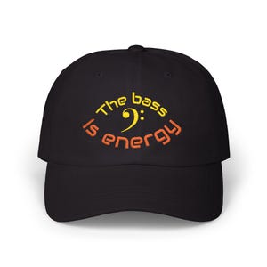Op de afbeelding: Zwarte baseballcap met de geborduurde tekst "The bass is energy" in geel en oranje. Het ontwerp bevat een vioolsleutelsymbool. Een stijlvol accessoire voor muziekliefhebbers.