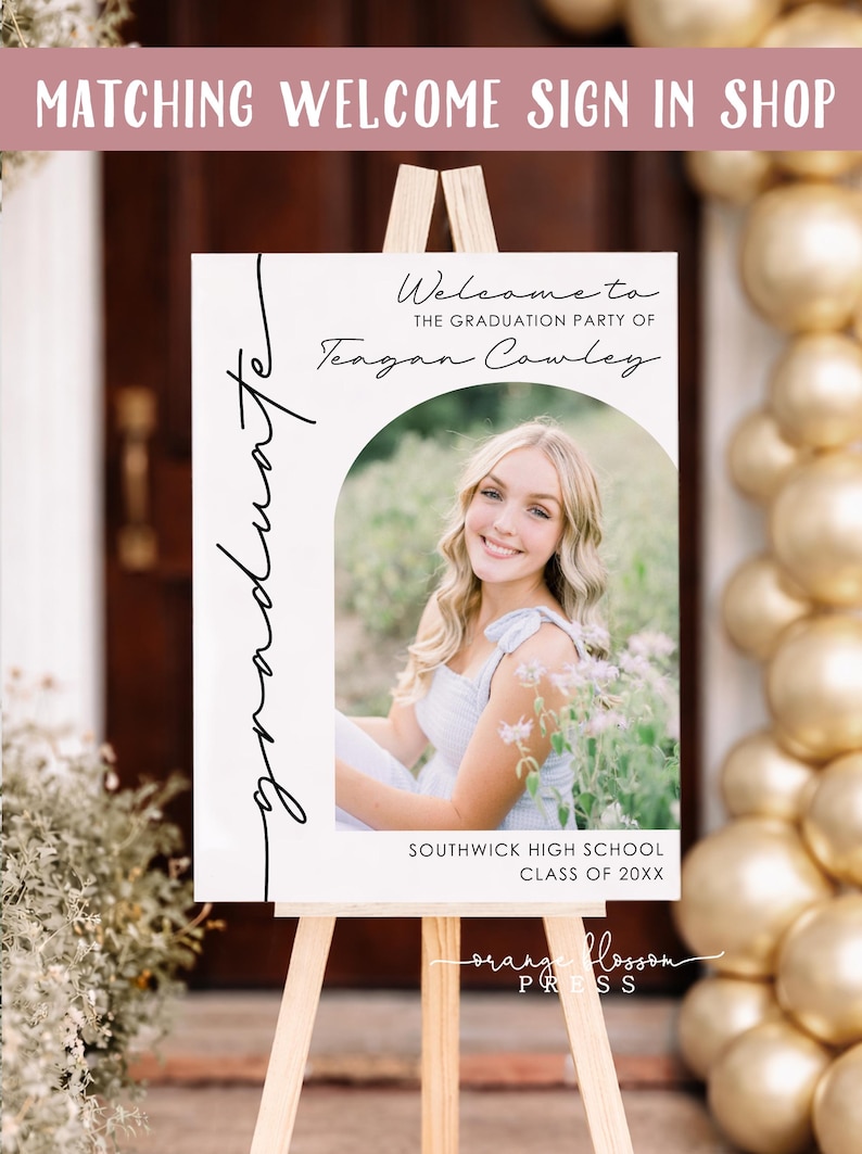 May include: A graduation party welcome sign on a wooden easel. The sign features a photo of a smiling person and the text "Welcome to the Graduation Party of Teagan Cowley." Additional text includes "Southwick High School Class of 20XX."
