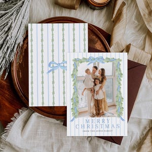 May include: Christmas card with a family photo, featuring a blue and white striped design with a watercolor garland and bow. The text reads "Merry Christmas from The Jones Family."