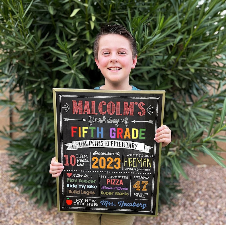 a young boy holding up a sign for a fifth grade class