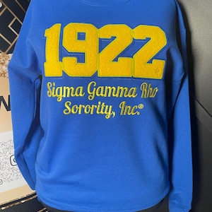 May include: A royal blue sweatshirt with a large yellow embroidered number "1922" and the text "Sigma Gamma Rho Sorority, Inc." in yellow embroidery.