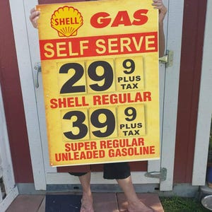 May include: A Shell gas station sign with the words "GAS", "SELF SERVE", and gasoline prices. The sign displays prices for Shell Regular and Super Regular Unleaded Gasoline. The sign is yellow with red and black text.