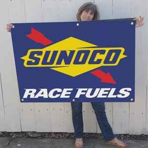 May include: A blue banner with the Sunoco logo in yellow and the words "RACE FUELS" in white. The logo includes a yellow diamond shape with the word "SUNOCO" in bold letters, and red arrows.