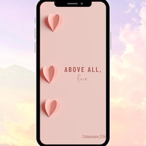 以下が含まれることがあります： スマートフォンは、3つの紙のハートが付いたピンク色の背景を表示します。「ABOVE ALL, love」というテキストは筆記体で書かれています。聖書の詩「コロサイ人への手紙3:14」が下にあります。電話には黒いベゼルが付いています。