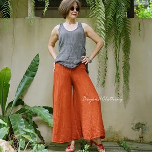 May include: A dark gray sleeveless tank top with a textured, crinkled fabric finish paired with wide-leg, burnt orange trousers featuring a smocked elastic waistband and a matching crinkled texture. The text BeyondClothing is visible on the pants.