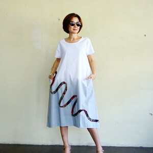 May include: White t-shirt dress with a light blue denim skirt. The dress features a decorative ribbon design in red, black, and green. The dress has pockets and is knee-length.