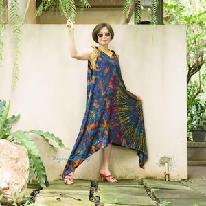 May include: A woman wearing a blue, orange, and red tie-dye maxi dress with a yellow sleeveless top underneath. She is wearing red sandals and sunglasses.