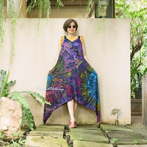 May include: A woman wearing a tie-dye maxi dress with a V-neck and a ruffled neckline. The dress is a dark blue color with shades of purple, green, and orange. The dress has a long, flowing skirt and a shorter front hemline.