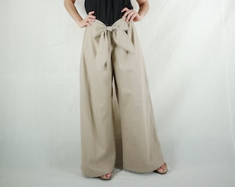 May include: Wide-leg pants with a large bow at the waist. The pants are a light beige color.