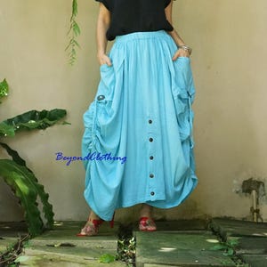 May include: A light blue maxi skirt with large pockets and a button-down front. The skirt has a gathered, voluminous design and is made of a lightweight fabric. The text "BeyondClothing" is visible on the skirt.