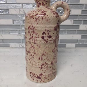 May include: A ceramic pitcher with a speckled brown and white glaze. The pitcher has a rounded body and a handle.