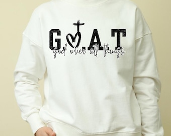 May include: White sweatshirt with black text that reads "G.O.A.T. god over all things" with a cross and heart graphic.