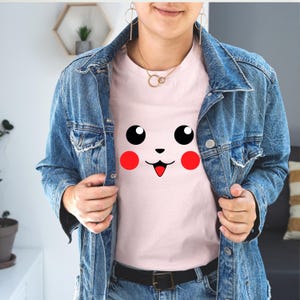 May include: A pink t-shirt with a cartoon face printed on the front. The face has large eyes, a small nose, and a wide smile. The face is red and white.