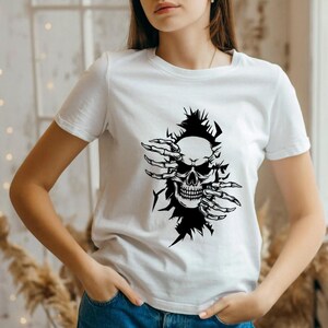 May include: White t-shirt with a black graphic of a skull with skeletal hands reaching out from behind it.