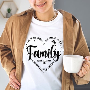 May include: White t-shirt with a black heart design that says "Family" with the text "Side by side... or miles apart... Will always be connected by heart".
