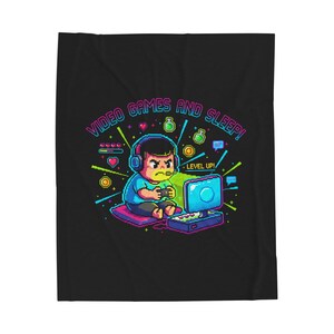 May include: A black blanket featuring a pixelated illustration of a person playing video games. The image includes the text "VIDEO GAMES AND SLEEP!" and "LEVEL UP!" in bright colors. The gamer is wearing headphones and has an angry expression.