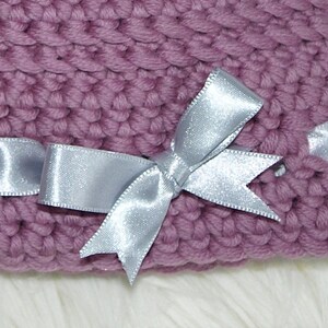 May include: A purple knitted hat with a silver satin ribbon tied in a bow.