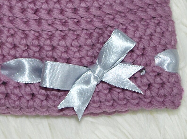 May include: A purple knitted hat with a silver satin ribbon tied in a bow.