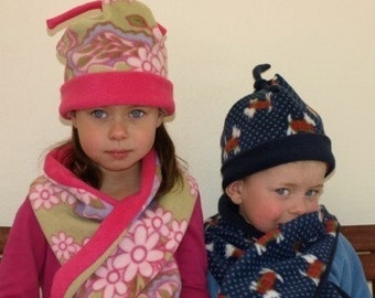 May include: Two children wearing colorful fleece hats and scarves. The girl's hat has a pink brim and a floral pattern. The boy's hat is navy blue with a white and red polka dot pattern. Both scarves are made of fleece and have a floral pattern.